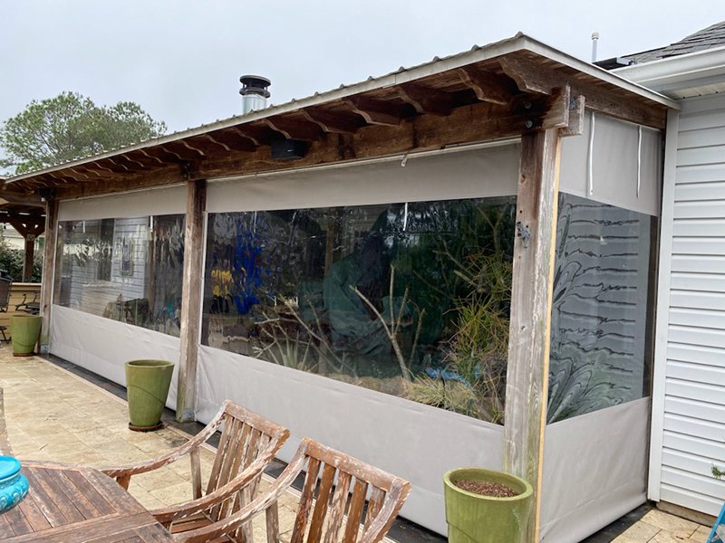 713D3B42-_800px Covered patio with clear plastic curtains and wooden furniture.